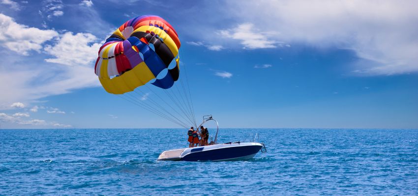 What is parasailing: colorful parachute towed by a boat with riders enjoying the ocean view.