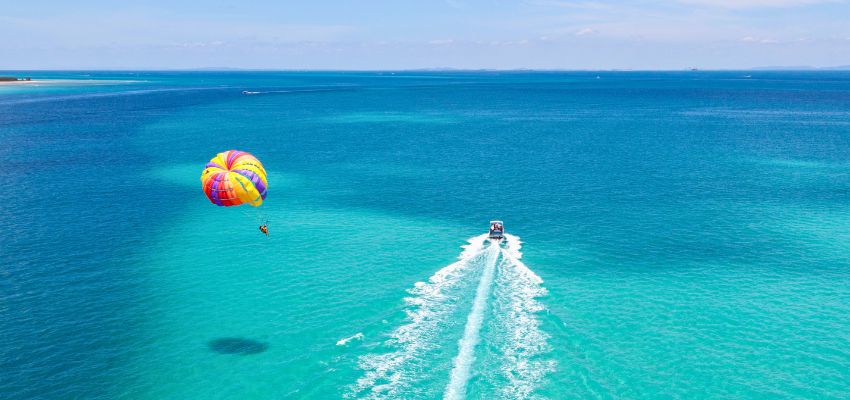 What is parasailing: aerial view of a boat pulling a parasailer high above turquoise tropical waters.