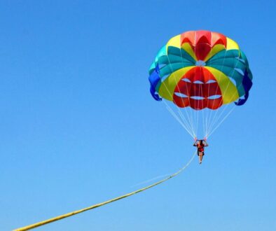 What is parasailing: person soaring under a vibrant colorful parasail against a clear blue sky.