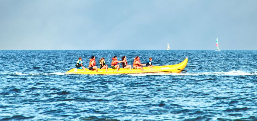 Group of people having fun on long yellow banana boat rides being pulled across the open sea.