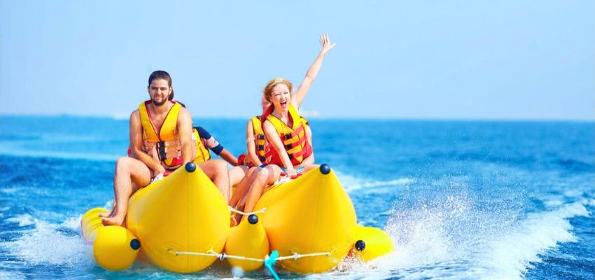 Smiling couple enjoying exciting banana boat rides on the ocean, woman waving with joy during the fun ride.