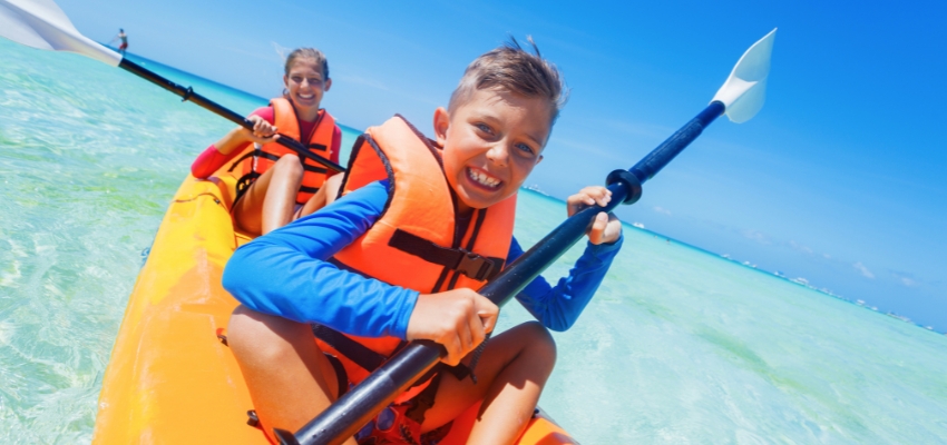 Smiling children kayaking on clear ocean water, enjoying water sports for kids