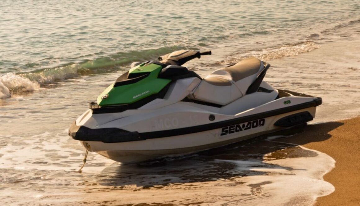 Green and white personal watercraft resting on the beach near gentle waves.
