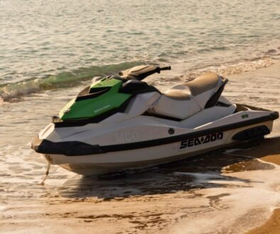 Green and white personal watercraft resting on the beach near gentle waves.