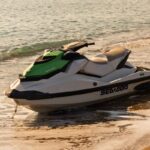 Green and white personal watercraft resting on the beach near gentle waves.
