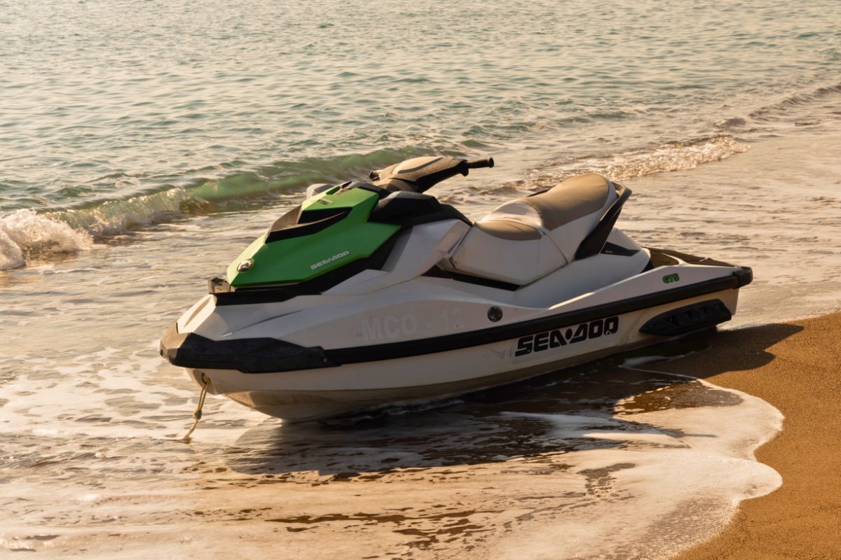 Green and white personal watercraft resting on the beach near gentle waves.