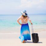 A woman holds her luggage while looking out over the beach on South Padre Island.