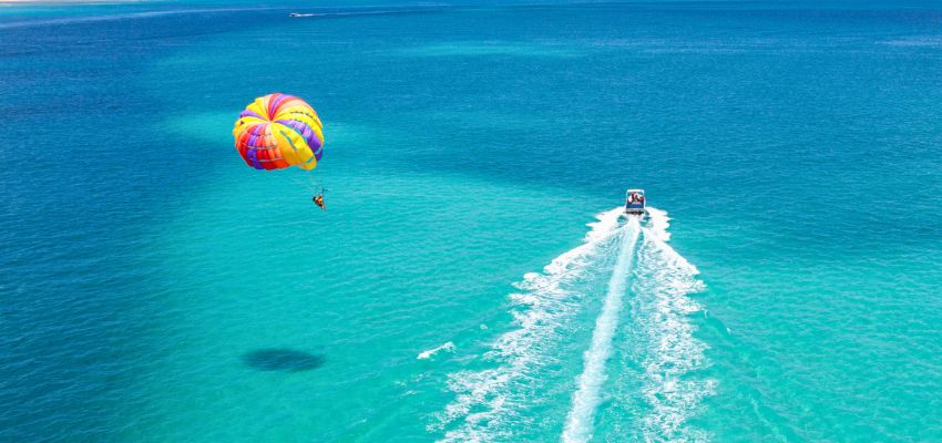 Aerial view of a colorful parasail being towed by a boat over turquoise waters, showcasing thrilling things to do in South Padre Island with family like parasailing adventures.