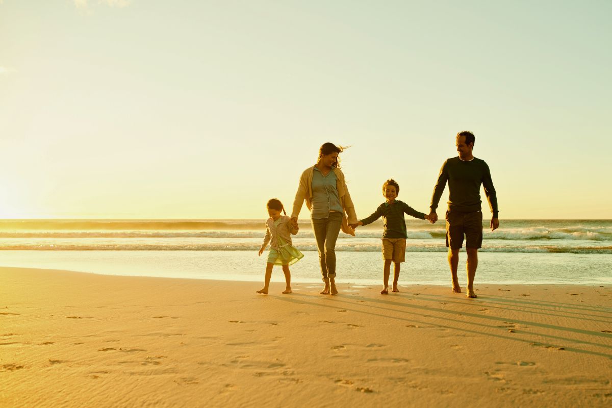 A happy family holding hands and walking along a sunny beach at golden hour, with gentle waves in the background, representing relaxing things to do in South Padre Island with family such as beach strolls.