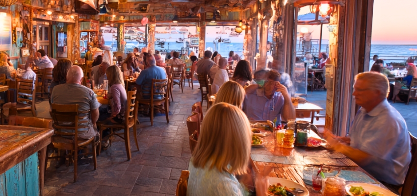 Vibrant, crowded waterfront restaurant filled with diners enjoying the sunset view, one of the best places to eat in South Padre Island.