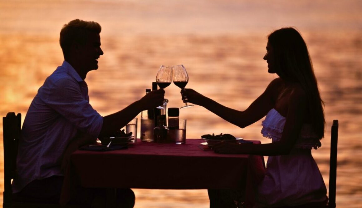 Romantic couple toasting with wine at a sunset beachside dinner, representing the scenic best places to eat in South Padre Island.
