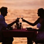 Romantic couple toasting with wine at a sunset beachside dinner, representing the scenic best places to eat in South Padre Island.
