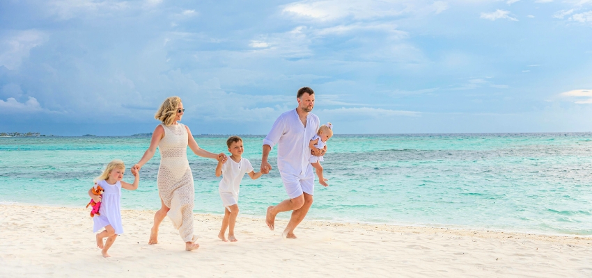Happy family running along a white sandy beach with turquoise waters, enjoying a perfect destination for where to travel in summer with kids