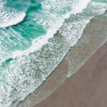 Turquoise waves crashing onto the sand in an aerial view, proving is there a beach in texas with beautiful shoreline scenery