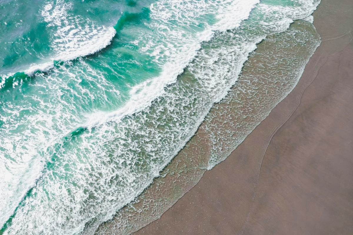 Turquoise waves crashing onto the sand in an aerial view, proving is there a beach in texas with beautiful shoreline scenery