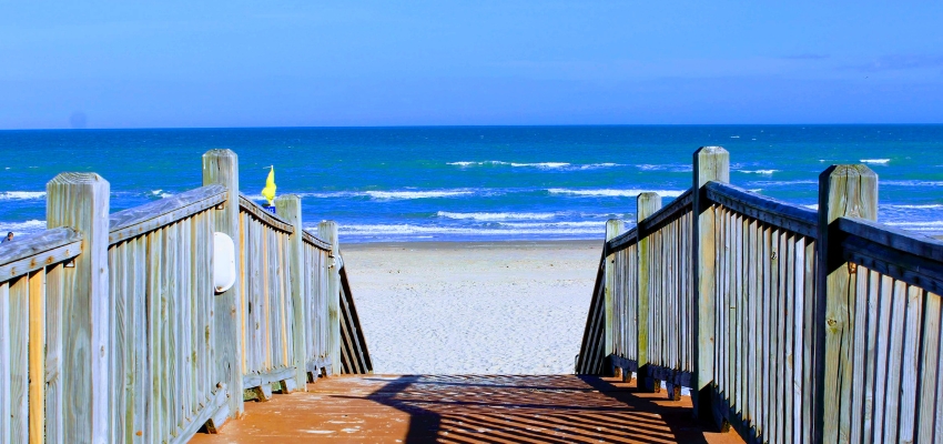 Wooden beach stairs leading down to the ocean and white sand, showing is there a beach in texas along the sunny coast