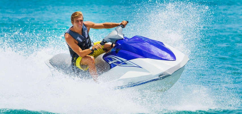Smiling rider speeding across turquoise water, demonstrating how to drive a jet ski.